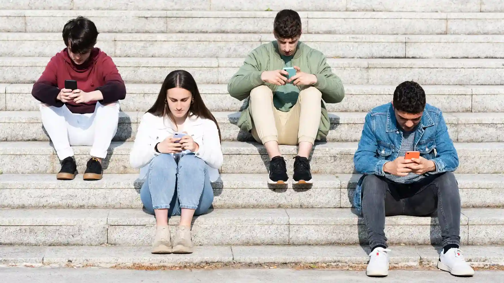 Jóvenes sentados consumiendo redes sociales en sus teléfonos móviles