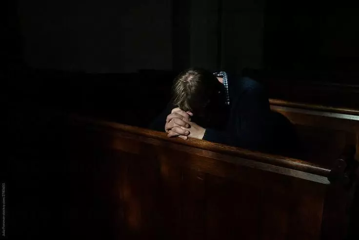 Persona orando de rodillas en iglesia